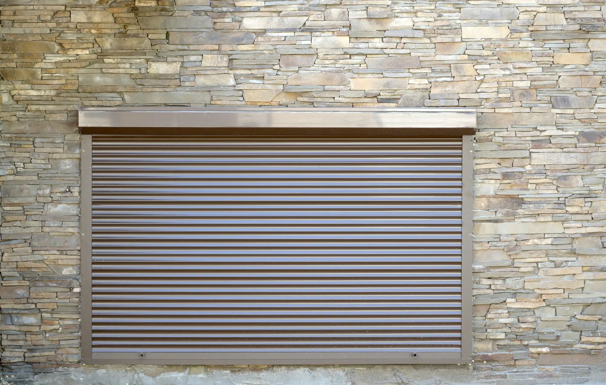 A window with brown metal rolling shutters. Wall decoration with artificial flatten stone