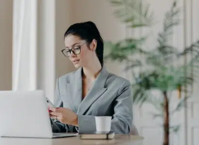 Gorgeous busineswoman types message on smartphone, works on new publication