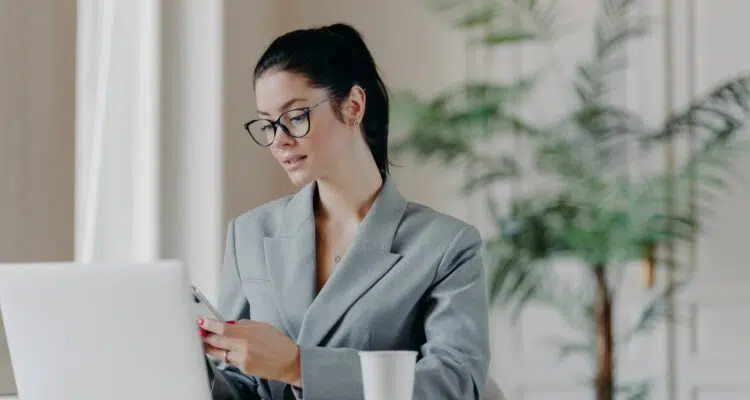 Gorgeous busineswoman types message on smartphone, works on new publication