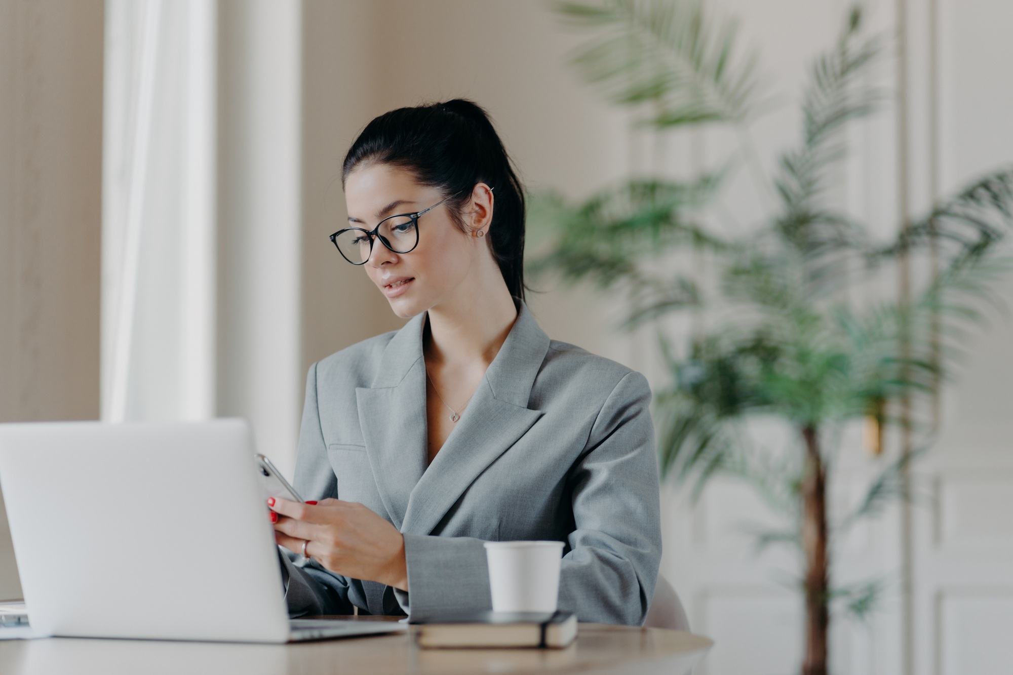 Gorgeous busineswoman types message on smartphone, works on new publication