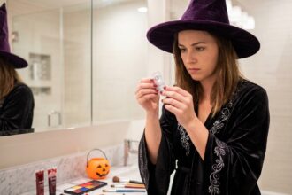 Jeune femme en costume de sorcière d'Halloween examinant un emballage de lentilles de couleur dans une salle de bain