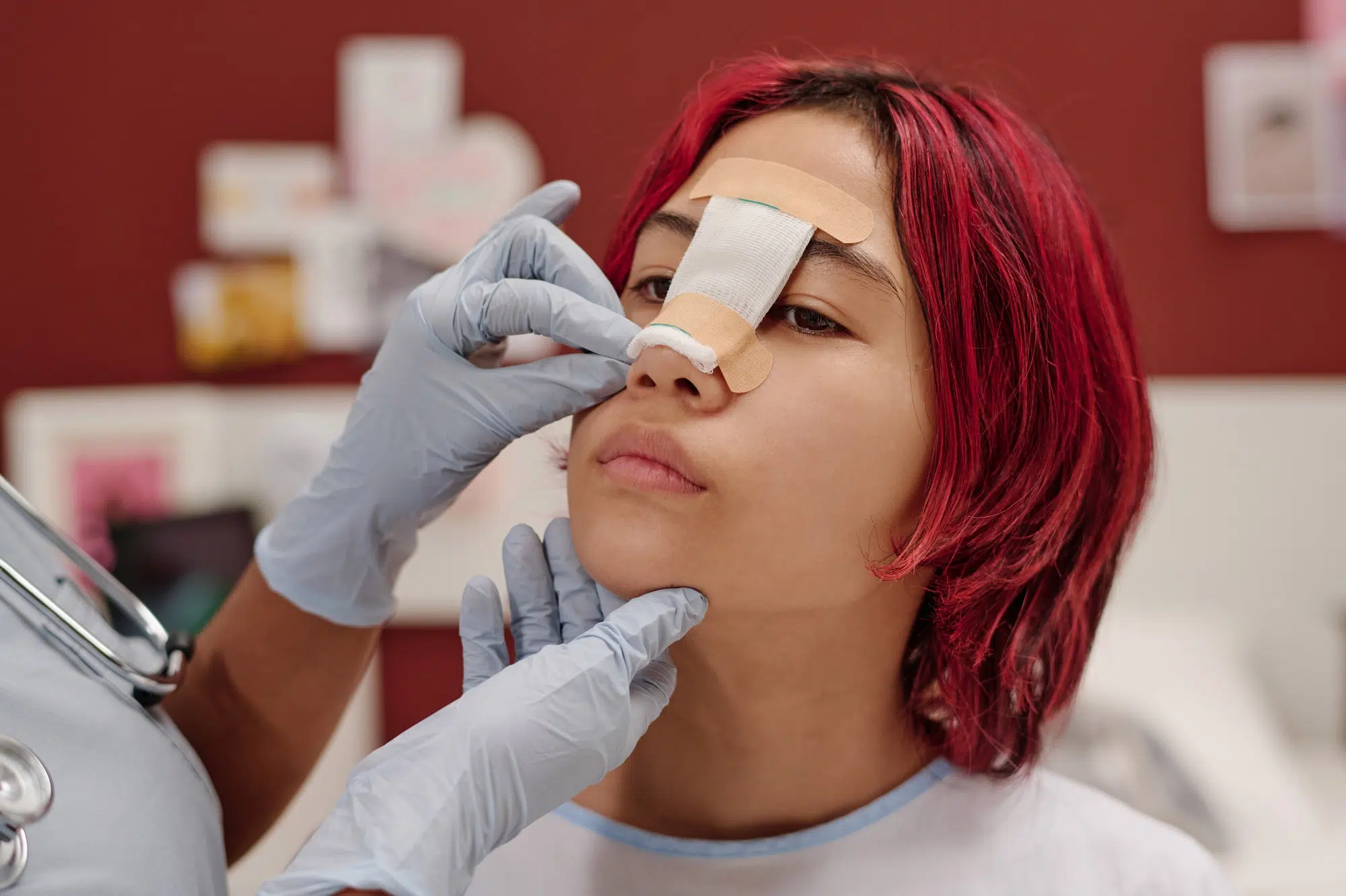 Plastic surgeon in protective gloves putting bandage on patient nose